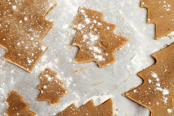 Gingerbread Cookie. New Year figures from a dough, prepared for baking in the oven. Cookies in the form of Christmas tree on paper for baking. Christmas food concept. Close up background. - Zdjęcie, obraz