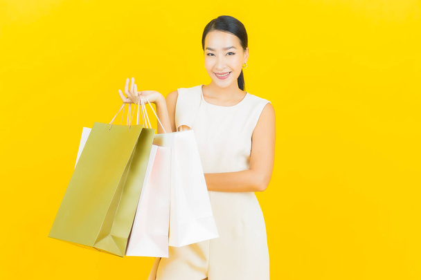 Portrait belle jeune femme asiatique sourire avec sac à provisions sur fond de couleur jaune - Photo, image
