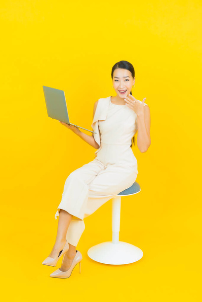 Portrait beautiful young asian woman smile with computer laptop on yellow isolated background - Fotoğraf, Görsel