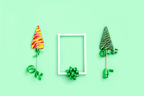 Lollipop shaped like Christmas tree. Creative New Year Flat lay with sweet candy lollypop with stripes on stick and white frame with copy space on neo mint colored paper background. - Fotografie, Obrázek