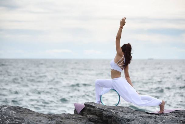 Junge Frau übt Yoga in der Natur Himmel & Meer Blick. Einfache Yoga-Posen für Anfänger mit Yoga Wheel am Abend, Stretching & Kräftigungsübungen mit fortgeschrittenem Yoga, Entspannungs- & Gesundheitskonzept. - Foto, Bild