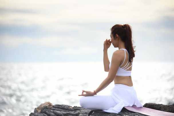 Sukhasana egzersizinde yoga yapan Asyalı genç bir kadın denize bakarken.... - Fotoğraf, Görsel