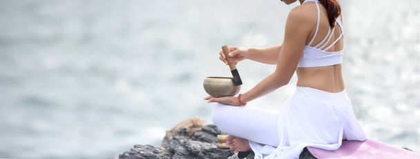 Asiatische junge Frau praktiziert Yoga, während sie auf einem natürlichen Meeresfelsen sitzt. Einfache Yoga-Posen für Anfänger. Trainieren Sie, während Sie auf das Meer blicken. Meditation mit Yoga. Bannergröße mit Kopierraum. - Foto, Bild