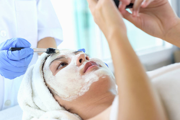 Jeunes femmes asiatiques recevant des soins du visage, des masques faciaux et des soins de beauté spa pour une peau douce et soyeuse par les esthéticiennes au salon de spa. Concept de soins de beauté - Photo, image