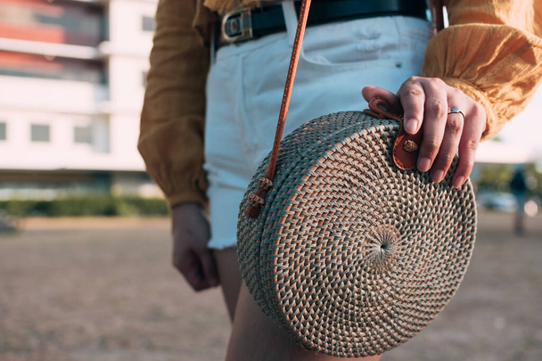 Egy nő egy Bali táskát cipel, miközben egy városi parkban sétál. Divatos rattan táska. - Fotó, kép