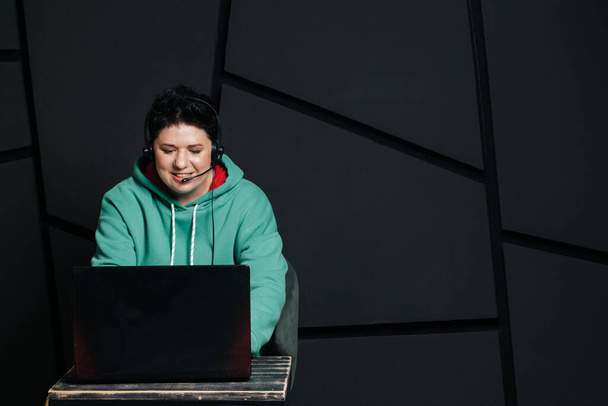 dispatcher, brunette girl with short hair wearing headphones at the computer, working online, on a dark background. - Foto, afbeelding