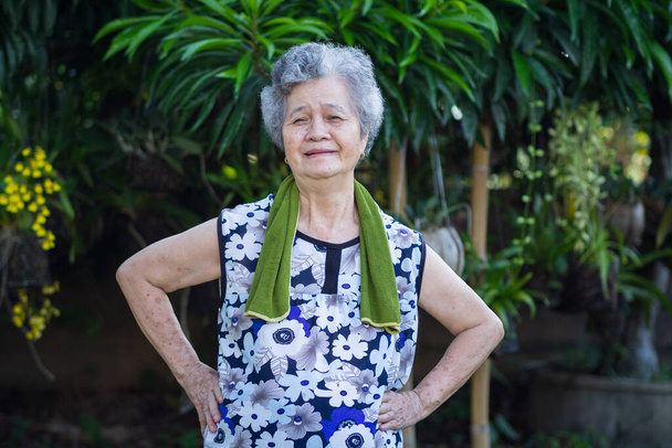 Portret azjatyckiej starszej kobiety ubranej w luźne ubrania, uśmiechniętej i ćwiczącej w ogrodzie. Piękne starsze kobiety krótkie włosy z siwymi włosami są szczęśliwe i zdrowe. Portret starszej kobiety - Zdjęcie, obraz
