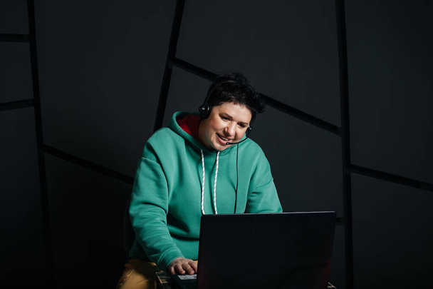 dispatcher, ragazza bruna con i capelli corti che indossa le cuffie al computer, lavora online, su uno sfondo scuro. - Foto, immagini