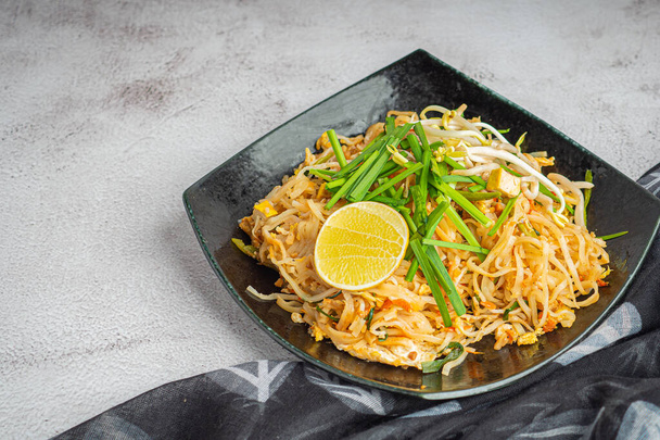 Pad Thai served with vegetables and lemon slices in black dish on gray cement background. Thai food famous. Side view with copy space. Concept of Thai traditional foods - Photo, Image