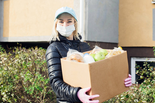 voluntária feminina vestindo uma máscara protetora caminha pela rua com uma caixa de compras, doações. - Foto, Imagem