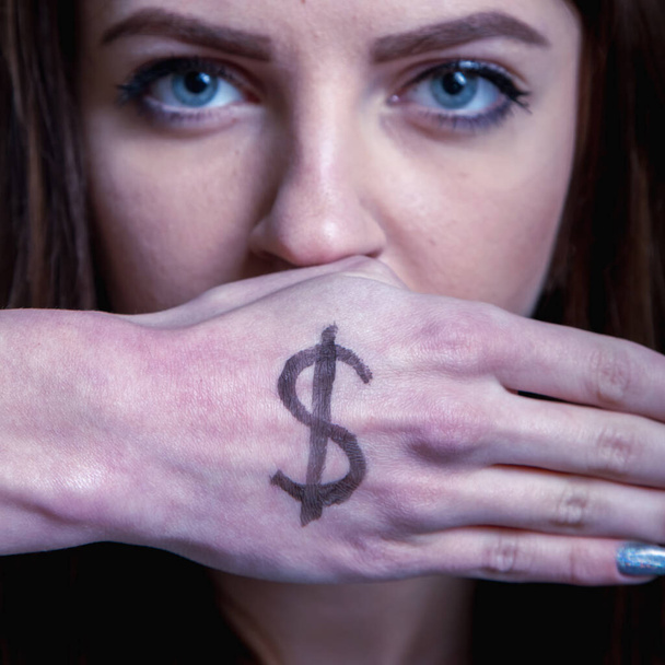 Usta młodej pięknej kobiety zamykają się dłonią symbolem pieniędzy. Przekupstwo, oszustwo, korupcja, finansowe i polityczne manipulacje. Selektywne skupienie uwagi na dłoni. - Zdjęcie, obraz