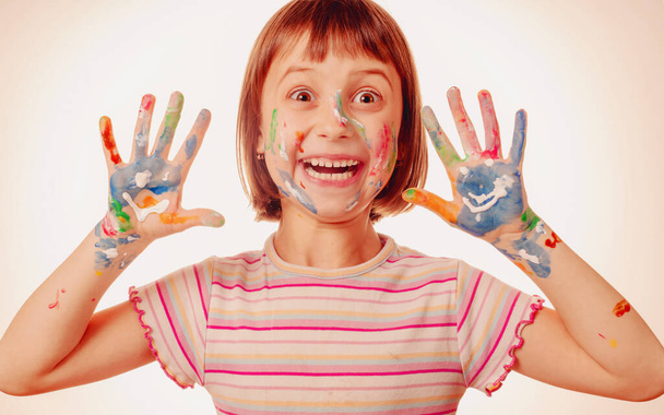 Funny facial expression of beautiful young child girl with colorful painted face and hands.  - Photo, Image