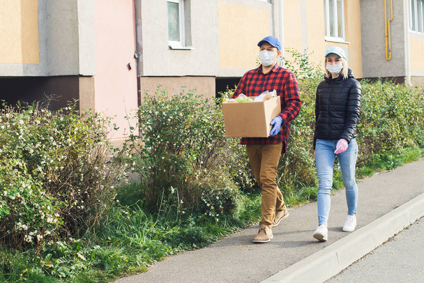 волонтеры в защитных масках идут по улице с коробкой продуктов, благотворительностью. - Фото, изображение