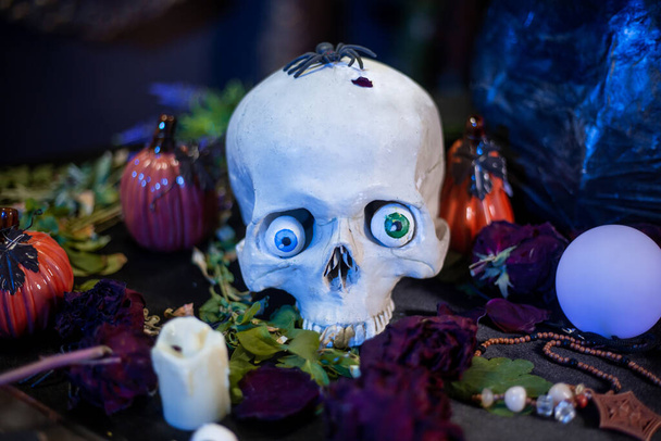 A human skull with multi-colored eyes lies on the table with the ingredients for witchcraft. Halloween witch altar concept. - Foto, imagen