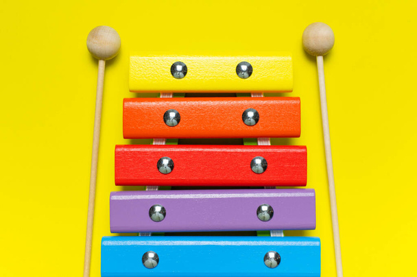 多色の木製の木琴と衝撃は、明るい黄色の背景フラットレイアウト上のビューのコピースペースに固執します。木製の子供の音楽おもちゃ赤ちゃん楽器虹の色。子供の自然エコおもちゃ. - 写真・画像