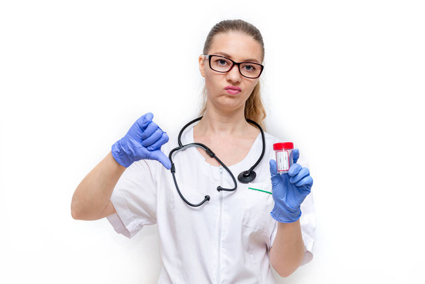 Female doctor in white coat and gloves holds container and shows thumbs down, bad analysis. White background. Timely medical exam and delivery of urine and Feces tests for prevention of diseases. - Fotoğraf, Görsel
