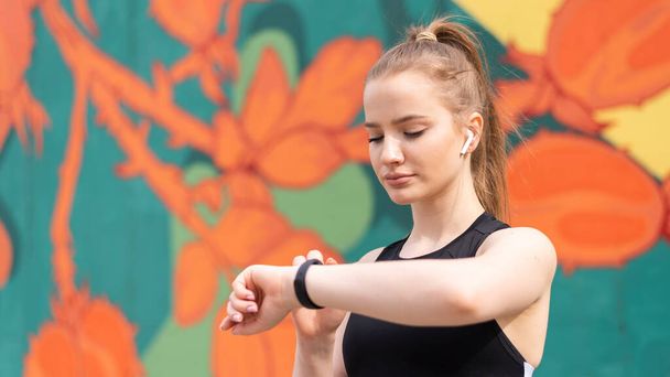 Jeune femme blonde à la formation en plein air en vêtements de sport est sur son bracelet de fitness, fond multicolore - Photo, image