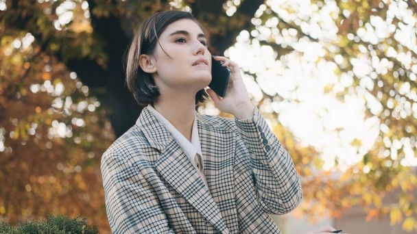 Attractive businesswoman looking confident talking on phone outdoor. Stylish girl making a business call working on cozy city street - 写真・画像