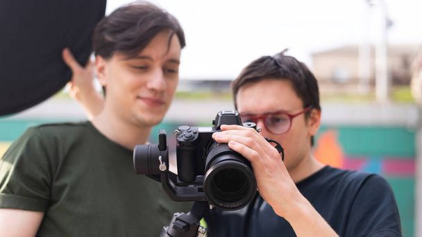Двоє молодих усміхнених фотографів дивляться на камеру на тринозі при фотосесії
 - Фото, зображення