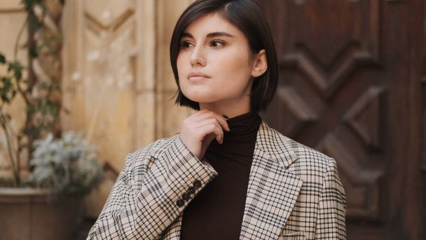 Attractive businesswoman dressed in plaid blaizer and turtleneck sweater looking confident waiting business meeting outdoor - Foto, afbeelding