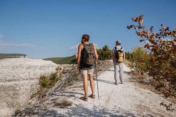 Due uomini che camminano su pendio roccioso portando zaini utilizzando bastoni da trekking. Montagne valle Vista accanto alla gente. estate viaggio nella natura - Foto, immagini