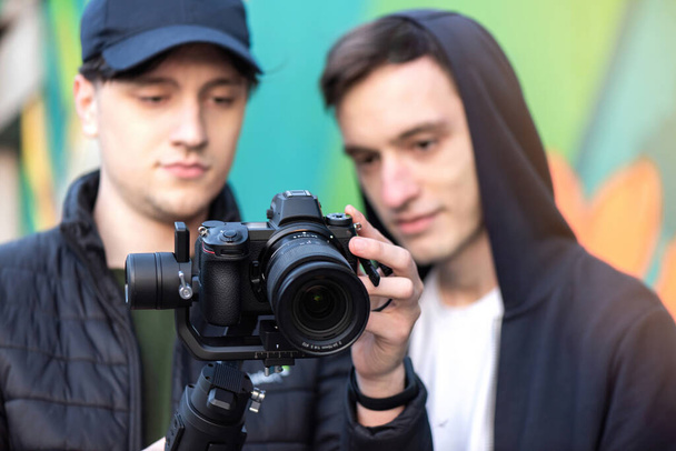Dois homens caucasianos olhando para a tela da câmera em um steadicam, fundo colorido - Foto, Imagem