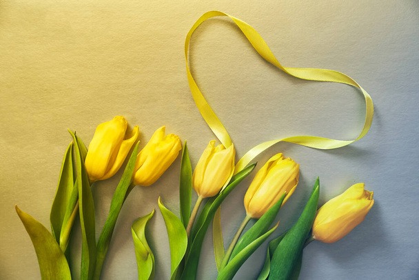 Пять желтых тюльпанов на желтом и сером фоне с сердцем из ленты - Фото, изображение