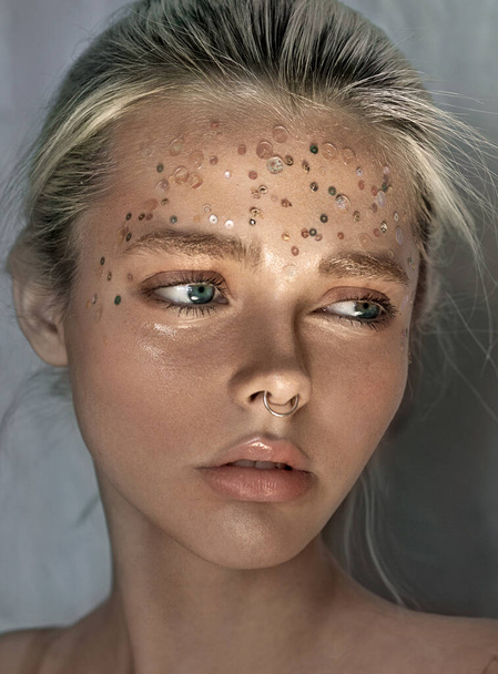 Close-up portrait of a girl. Sequins and beads on the face. Concept. Nose piercing. Earring is a ring. - Фото, зображення