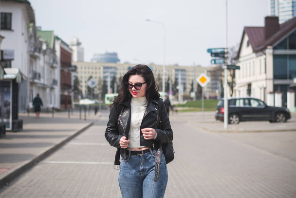 A beautiful hipster girl with a phone in her hands walks down the street on a sunny spring day - Foto, imagen