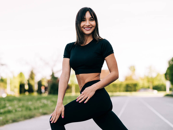 Young fitness girl doing stretching exercise outdoors on a sunny day and smiling. Happy fitness healthy lifestyle concept. - Foto, Imagen