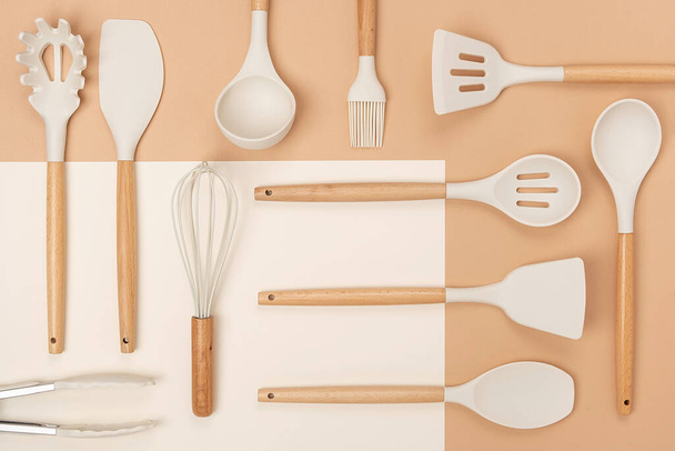 Pattern made from cooking utensil set. Silicone kitchen tools with wooden handle on beige background. Top view Flat lay. - Фото, зображення
