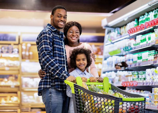 Portret radosnej afroamerykańskiej rodziny z uroczą córką pozowanie i uśmiech przed kamerą w dużym supermarkecie - Zdjęcie, obraz