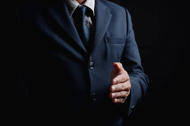 Close-up foto van een zakenman in een pak op een zwarte achtergrond, Zakenman met een lege hand met kopieerruimte. - Foto, afbeelding