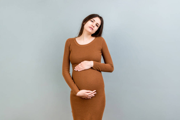 a pregnant girl who has a stomach ache stands on a colored background. isolated. - Foto, Imagen