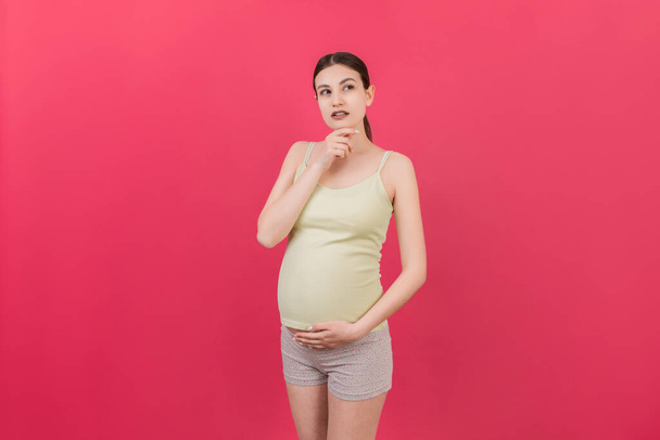 Pensieve zwangere vrouw kiezen naam voor baby op gekleurde achtergrond. Droom en gelukkige zwangere vrouw denkend aan het moederschapsleven. Kopieer ruimte.. - Foto, afbeelding