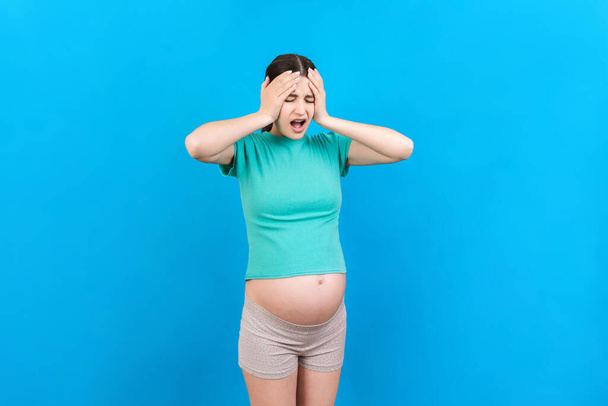 Schöne junge schwangere Frau mit Kopfschmerzen auf farbigem Hintergrund isoliert. Gestresste Schwangere oder Probleme mit der Mutter. - Foto, Bild