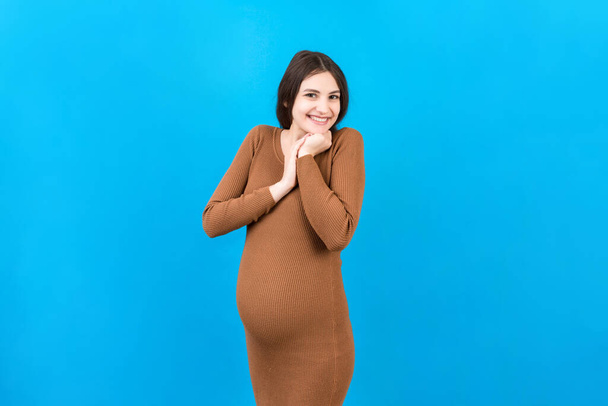 Happy pregnant woman touching her abdomen at Colored background. Future mother. Expecting of a baby. Copy space. - Φωτογραφία, εικόνα