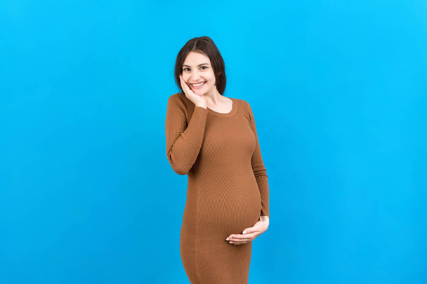 Mujer embarazada feliz tocando su abdomen en fondo de color. La futura madre lleva ropa interior blanca. Esperando un bebé. Copiar espacio. - Foto, Imagen