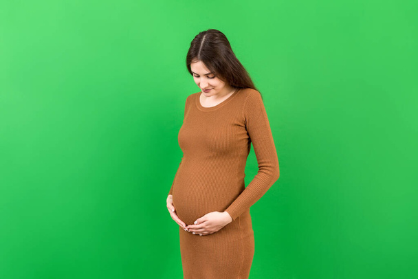 Happy pregnant woman touching her abdomen at Colored background. Future mother. Expecting of a baby. Copy space. - Photo, Image