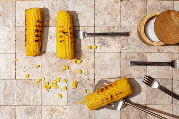 Pyszne organiczne domowe gorące kolby kukurydzy na ziemi stonowane opowieści tło widok z góry serwowane z płatków soli w widelcach - Zdjęcie, obraz
