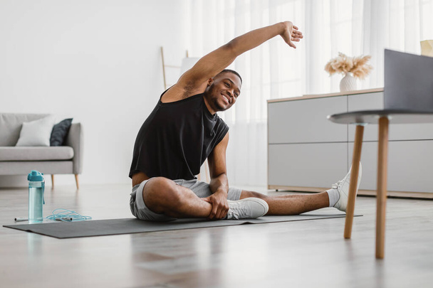 Веселый черный человек делает боковой изгиб растяжения упражнения дома - Фото, изображение