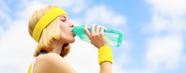 Egészséges életmód koncepció. Iszogattam sport közben. Egy fiatal nő vizet iszik futás után. Egy sportruhás nő egy üveg vizet tart a kezében. Sport lány iszik vizet egy üveg az égen háttér - Fotó, kép