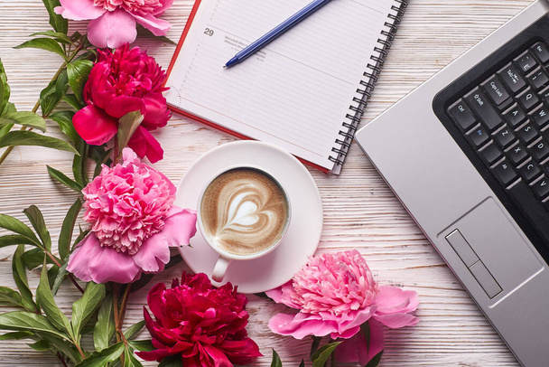 フラットレイアウトの女性のオフィスデスク。ノートパソコン付きの女性ワークスペース、ピンクの牡丹の花束と白い背景のコーヒー。トップ表示女性の背景. - 写真・画像
