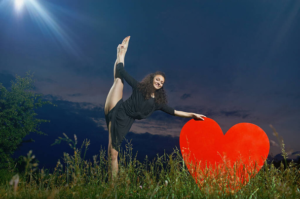 smiling, curly dancer performs vertical side splits in grassy field - Foto, imagen