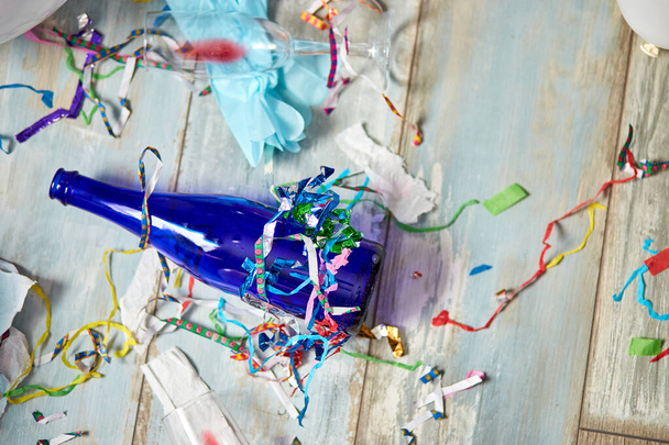 Вид зверху на підлогу після святкування вечірки з порожніми блакитними пляшками, келихом вина та вечірніми прикрасами, безладним інтер'єром вітальні, після вечірнього хаосу, дня народження
 - Фото, зображення