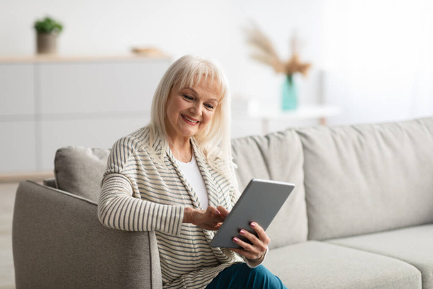Lächelnde reife Frau sitzt mit Tablette auf Couch - Foto, Bild