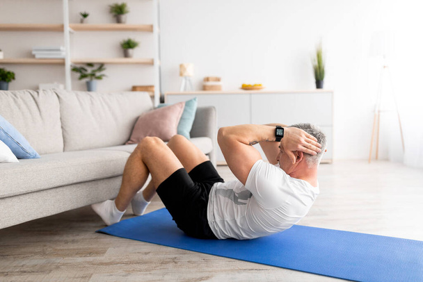Ćwiczenia w domu. Dojrzały mężczyzna robi mięśnie brzucha w pobliżu sofy, ćwiczenia w salonie w domu - Zdjęcie, obraz