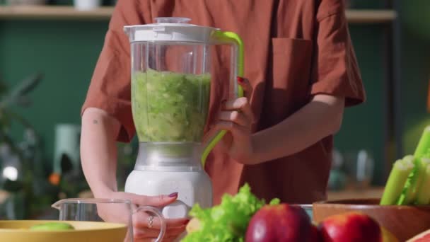 Ενδιάμεση λήψη αγνώριστης γυναίκας που ανοίγει το μπλέντερ και φτιάχνει πράσινο smoothie από φρέσκα λαχανικά και φρούτα στην κουζίνα στο σπίτι - Πλάνα, βίντεο