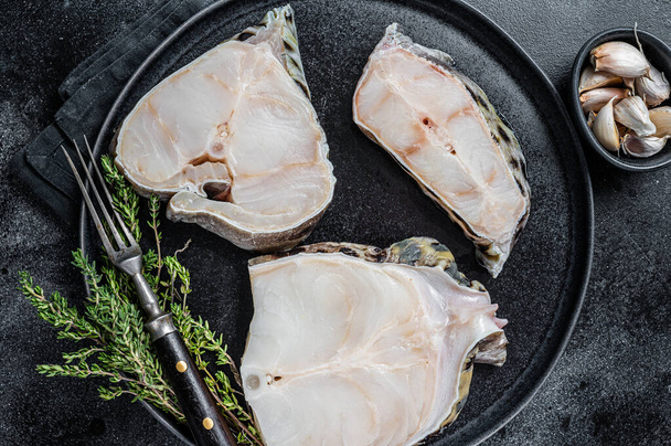 Fresh Raw wolffish o wolf fish Steak on a plate. Black background. Top view - Photo, Image