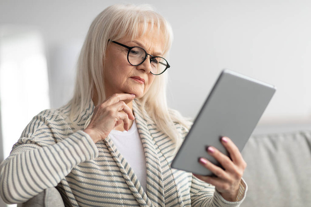 Mature woman using tablet sitting on couch - Photo, image